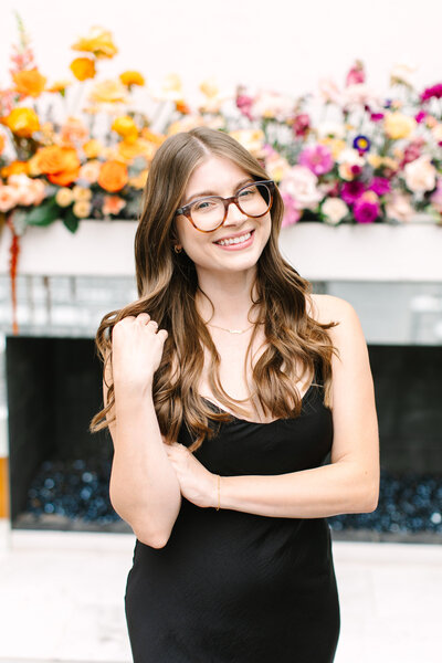 Sydney Russo, senior event sales coordinator at SoHo63, a Chandler wedding and event venue, smiles in front of a lush floral arrangement. Her warm, professional presence represents the expert planning and personalized service SoHo63 offers for weddings and events.