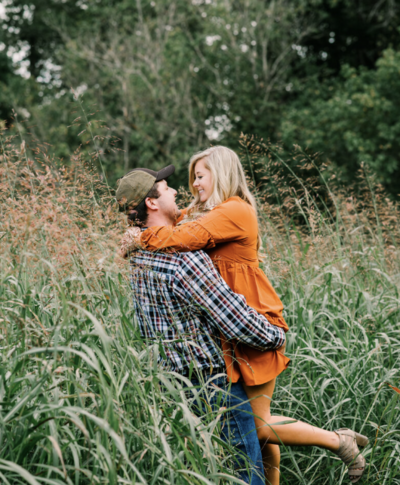 Woman embraces fiance in orange dress for engagement session.