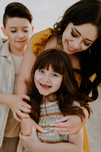 mom hugging a smiling little girl from behind while her some watches over her shoulder on a country road in decatur, tx