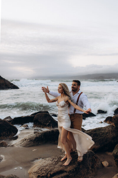 A couple stands on rocks, embracing each other, with the vast ocean as their backdrop on their wedding day in San Francisco bay area