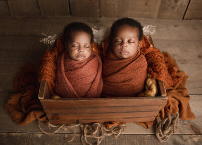 twin boys wrapped in orange in a basket