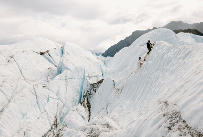 Bride in a wedding dress ice climbing on a glacier in Alaska, roped in with her partner during their adventurous elopement.