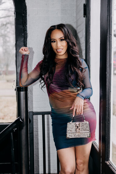 Flash photo of Tiara in a multicolored dress holding a snakeskin purse