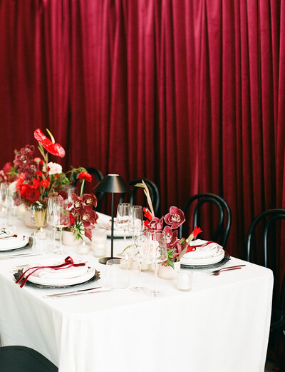 Bride and groom sitting at reception table and smiling while woman stands in front of them