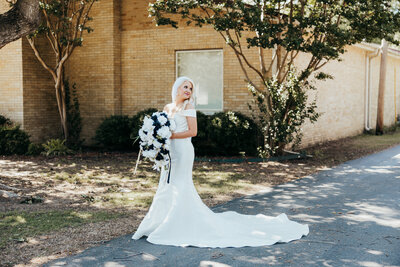 The bride's side profile standing in front of the church with her dress train fluffed out trailing behind her and looking behind over her shoulder