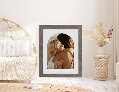 Mock up of wall art a little blonde girl resting her head on her mum's shoulder as they hug.