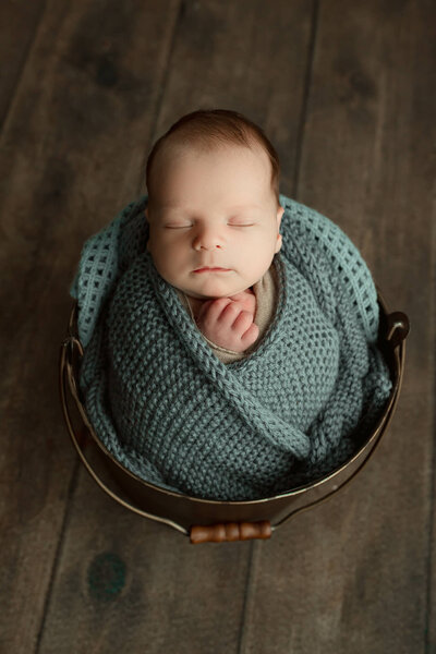 Peaceful slumber of a newborn baby swaddled in a knit blanket with a matching bonnet, cradled in tranquility during a Harrisburg studio newborn photo session.