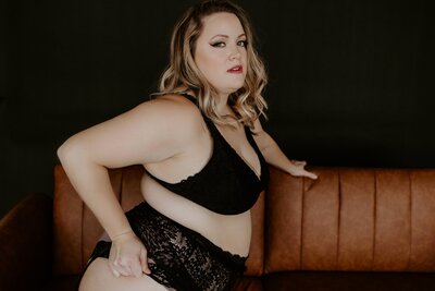 plus size woman sitting on a leather couch in black lingerie