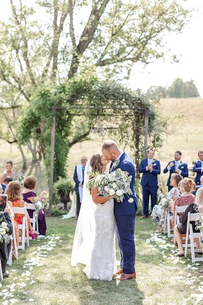 Bride and groom kissing in the middle of wedding aisle as they walk down the aisle