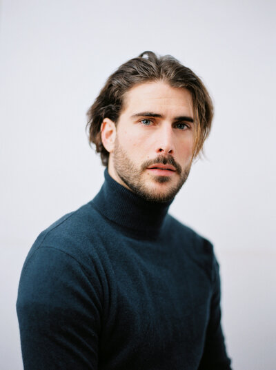 Man sits for portrait in navy turtleneck sweater