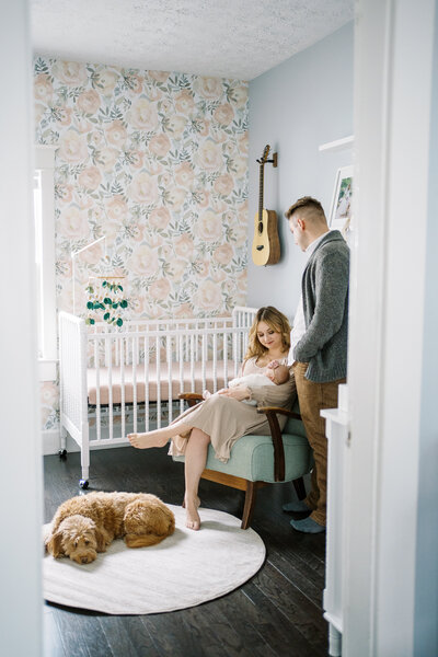 parents and dog watching over newborn baby in their nursery