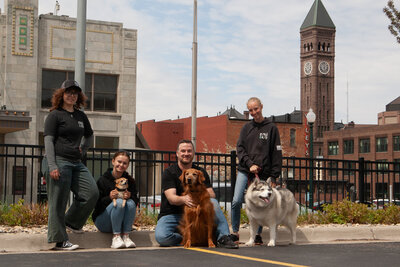 Roxi & Co team members with their dogs in front of the Sioux Falls skyline — locally owned, community-driven pet store.