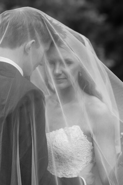 A black-and-white photo of a groom lifting his bride off the ground as they gaze at each other with love. The slight angle adds a spontaneous, candid feel.