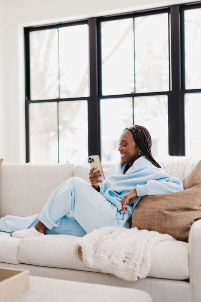 Juma Waganda in a light blue sweatsuit holding her phone sitting on the couch