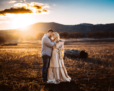 Family Photographer, a couple embrace at sunset in a meadow