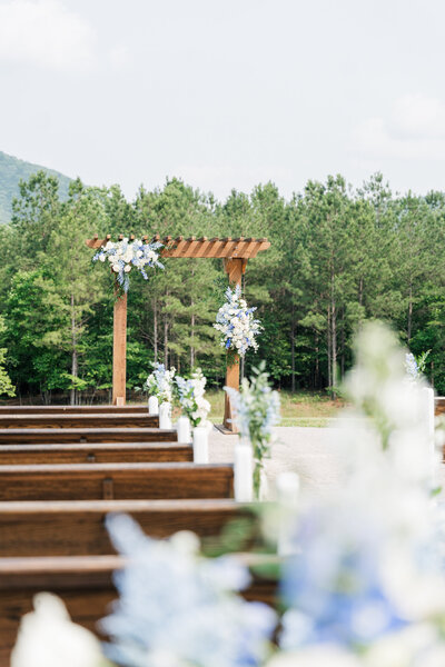 The aisle at a wedding leading to the arbor covered in florals with a backdrop of trees. 