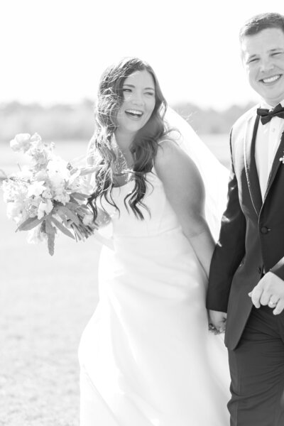 Laughing bride in strapless gown walking hand in hand with groom in tux