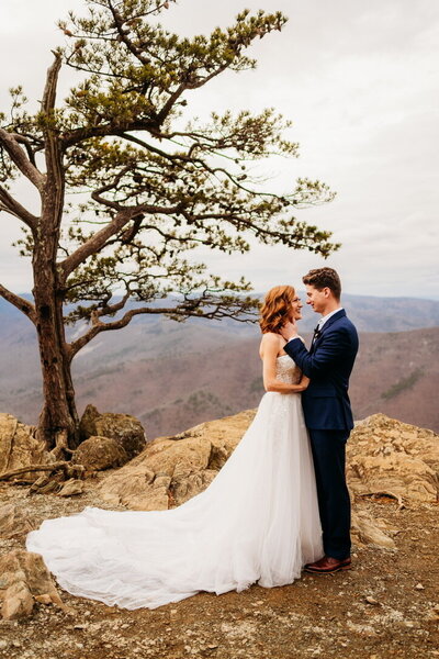 Couple embracing at the edge of a cliff with dramatic mountains behind them during a dreamy mountain elopement