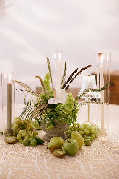 Flower center pice in a cement vase surrounded by grapes, kiwi, and pears. Along with candles and votives.   