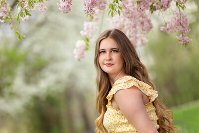 Senior girl standing in front of blooming cherry tree in downtown Boise during senior pictures with Tiffany Hix Photography