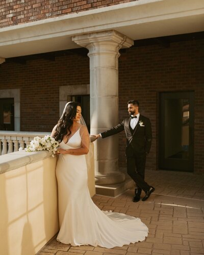 bride and groom standing on balcony near  stone column