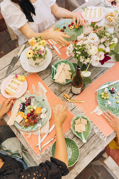 Top down view of an outdoor table,. Tabletop has florals, wine, and light summer food.