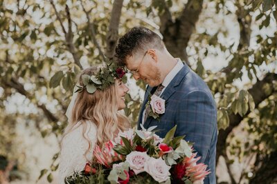 Bride and groom stand facing each other with their foreheads resting together for a wedding day portrait at The Clearing in Shedden, just outside of London, ON. The bride is wearing a floral crown. Her bouquet is in front of them in the foreground.