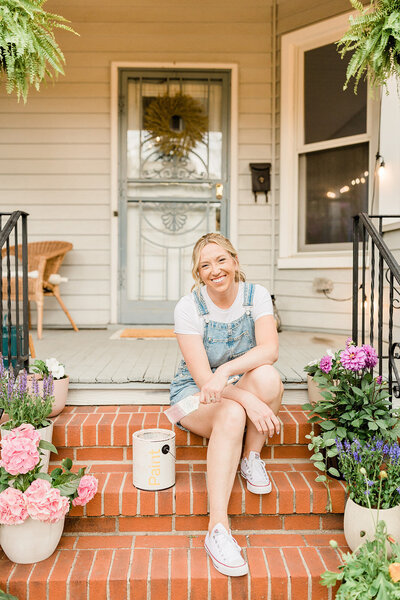 Jennifer Hardin sitting on the front porch of her victorian home with a paint can beside her.