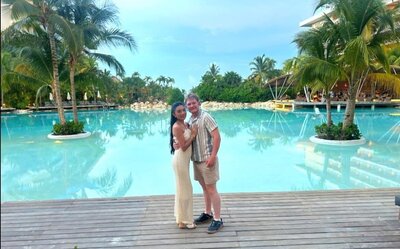 Photo of couple standing by tropical resort pool with personal vacation planner for destination weddings