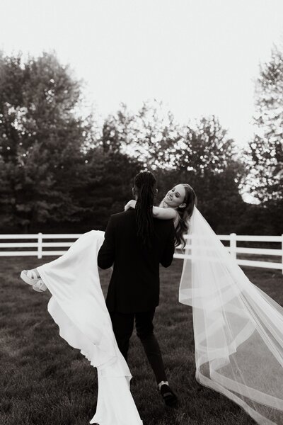 black and white photo of groom carrying bride