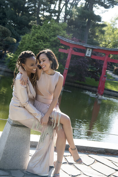 A person sitting on their partner's lap as they sit by a pond. 
