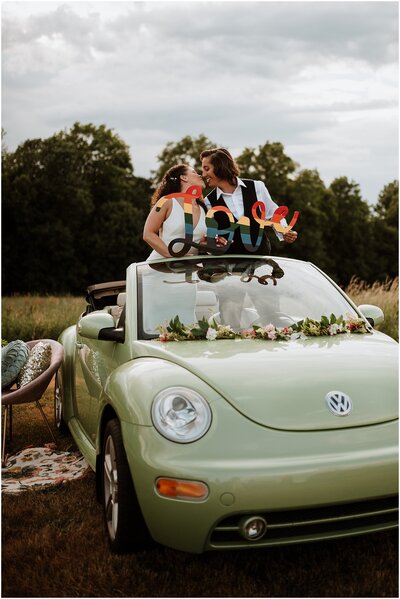 vintage sage green VW bug photobooth with brides  inside holding a rainbow "love" sign
