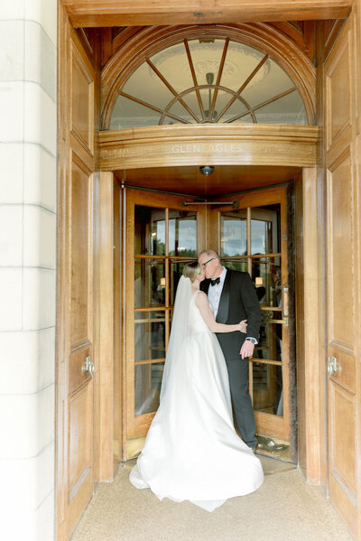 Bride and Groom kiss in the turnstile doorway of Gleneagles Hotel on their wedding day. Image by award winning luxury wedding photographer Scotland, Jill Cherry Porter.