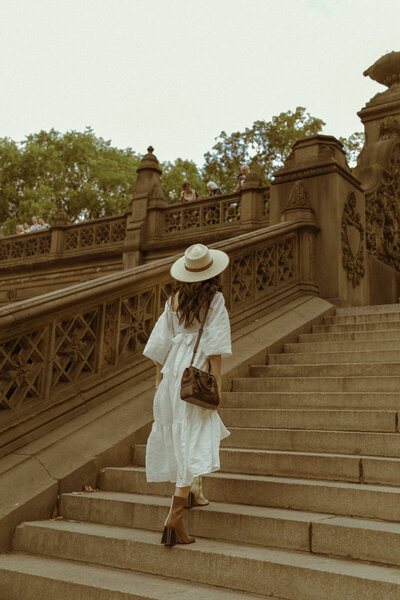 Woman in a white summer dress, straw hat and boots, walking  up the steps at the Bestheda Fountain in Central Park, NYC
