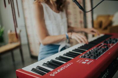 A person playing a red Nord Electro 5 keyboard in a room with a beige and brown background, evoking the creativity often seen in Shreveport web design.