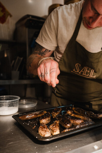 Chef seasoning roasted vegetables on a tray while wearing a Sael Birmingham restaurant apron.