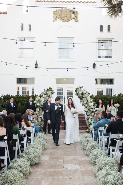 A couple walking down the aisle as husband and wife. Classy black tux and timeless wedding dress. Bi-racial weddings. Asian wedding.