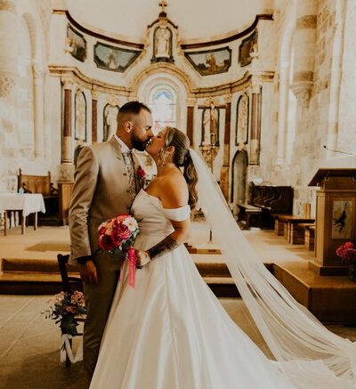 Gros plan sur les tenues des mariés se tenant par la main. Robe courte blanche pour elle et costume rose pour lui. Immortalisé par Laura, photographe en Vendée.