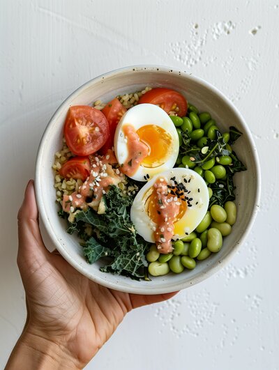 an egg and veggie bowl, held by a hand in front of a white background