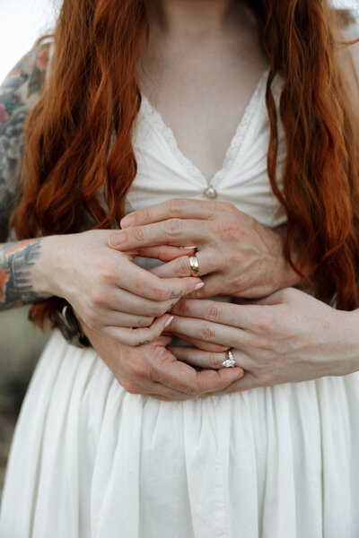 A close up image of a couples hands holding each other's wedding rings in the Arizona Desert.