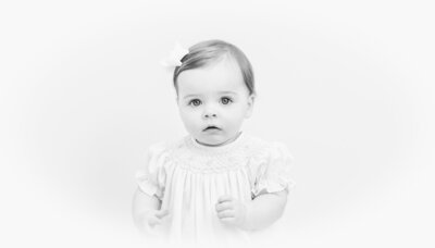 Black-and-white heirloom portrait of a toddler girl in a smocked dress.