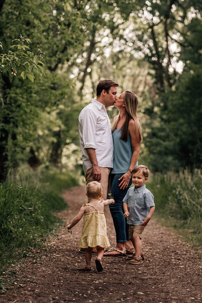 A couple stands and kisses at Lyndale Park Gardens in Minneapolis, while their daughter runs up to give a flower to their young son who is standing in front of them.