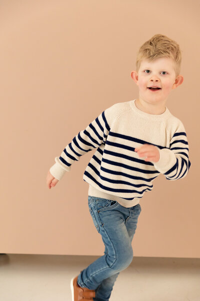 toddler boy looks into camera as he starts to run off to the right side of frame, smiling