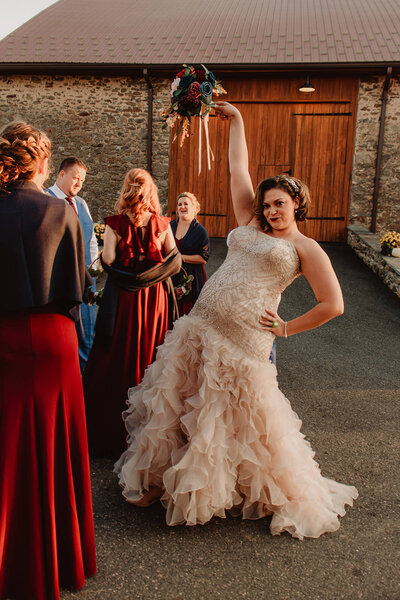 A person in a wedding dress with one hand up holding a bouquet and another on their hip
