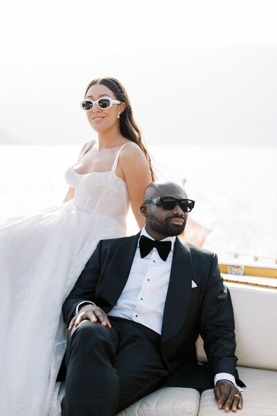 Bride and groom in sunglasses posing confidently on boat, chic destination wedding in Montenegro