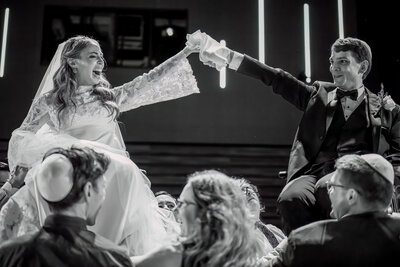 Bride and groom lifted on chairs during hora dance at Prosserman JCC wedding
