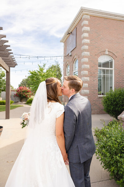 Young LDS bride and groom sharing a kiss outside of Talia wedding venue in Clearfield UT