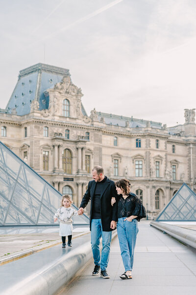 Mother, father and daughter walking by Louvre Pyramids during family photoshoot in Paris