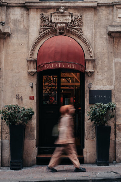 An entrance to a place that's name looks to say Galata in a very old building with a beautiful  decorative arch top and a red round canopy over the door
