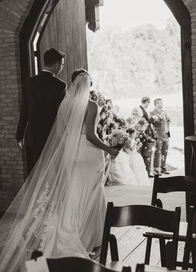 Just married couple exits The Little Chapel at Haven Ridge as guests celebrate with bubbles in Winston-Salem, North Carolina.